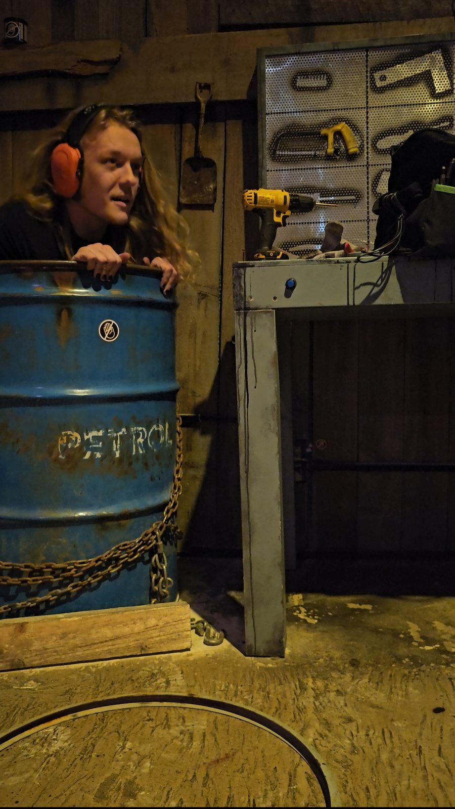Robert crouched behind a blue petrol barrel in a room set